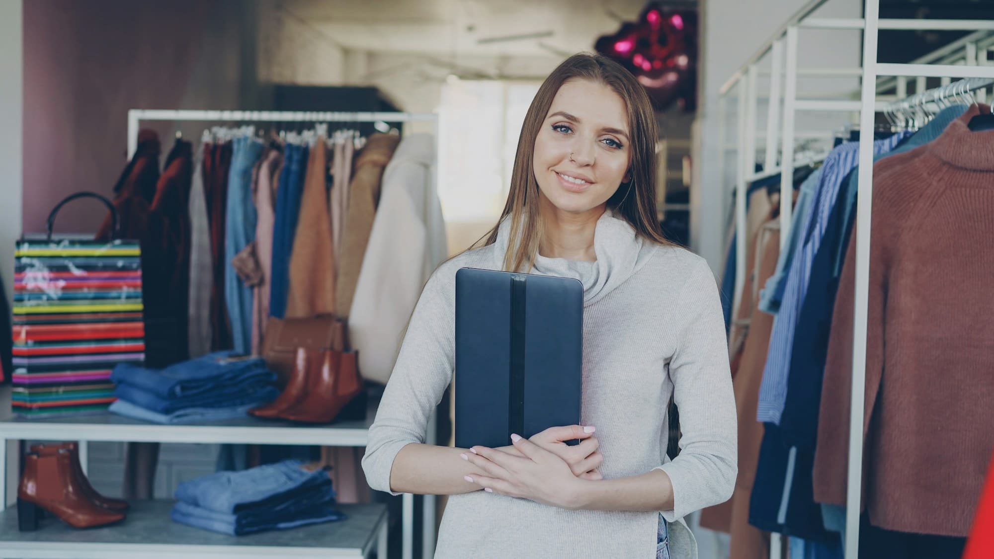 A boutique owner holding a tablet in her clothing shop